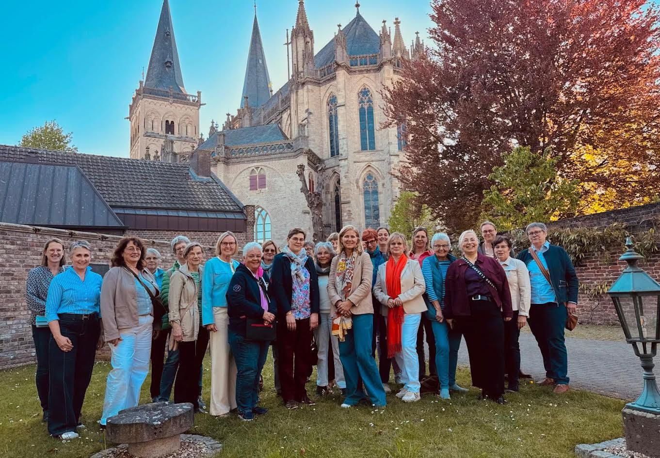 Gruppe von Menschen vor historischer Burg mit mittelalterlichem Bau, sonnig und freundlich.